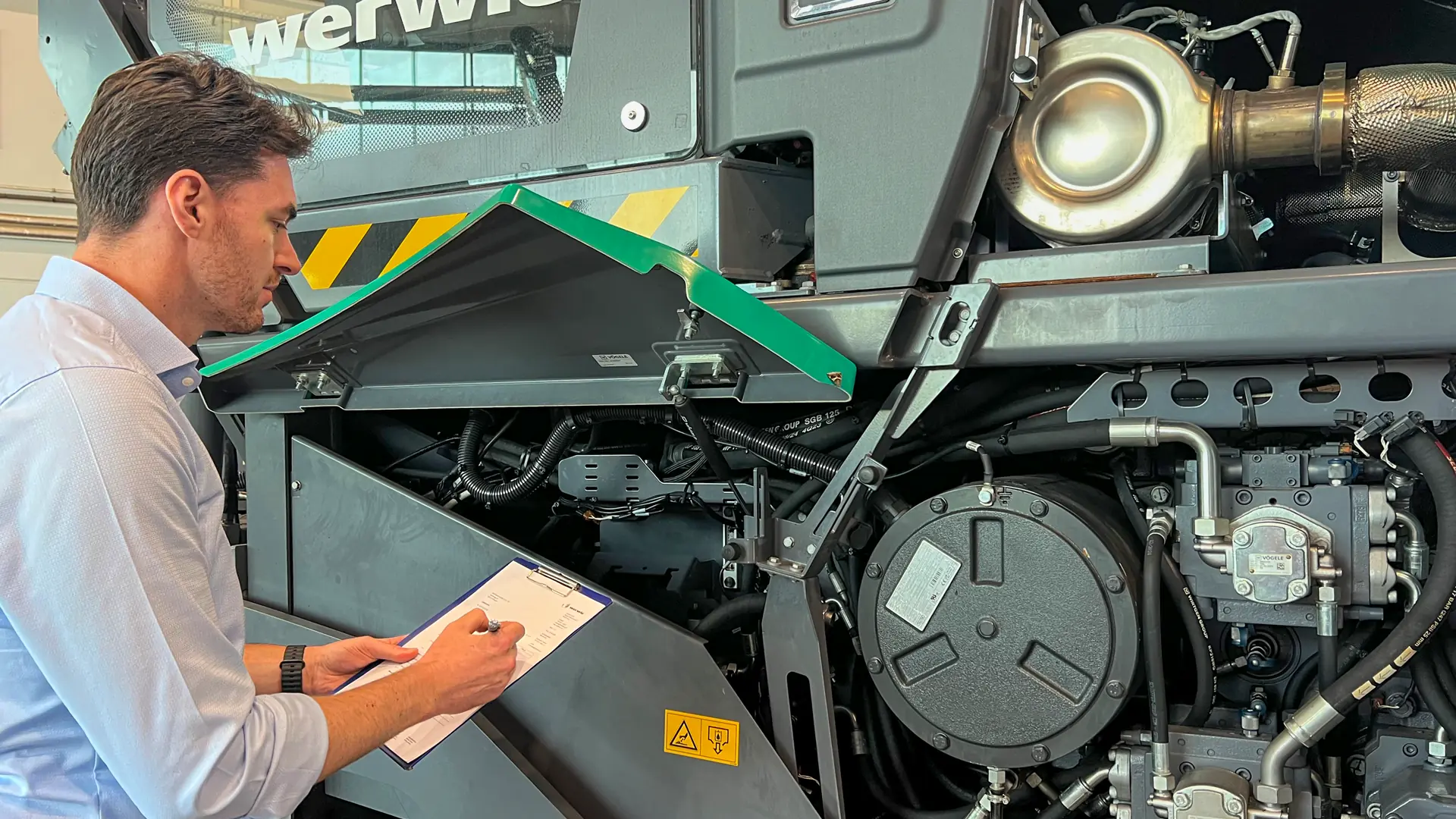 werwie Experte bei der detaillierten Maschinenbewertung und technischen Zustandsprüfung einer Baumaschine mit Klemmbrett.